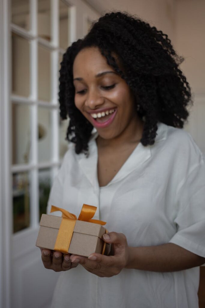 Smiling woman with curly hair receives a gift with orange ribbon, capturing happiness indoors.