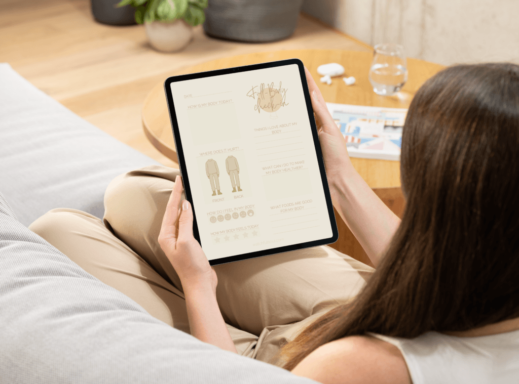 A person seated on a couch, using the ‘full body check-in’ journal on a tablet to track physical sensations and self-care needs.