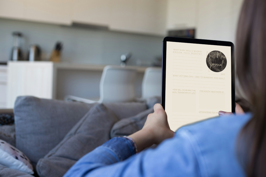 A person relaxing at home, using a tablet to complete the ‘new moon journal,’ focused on setting intentions for the upcoming lunar cycle.