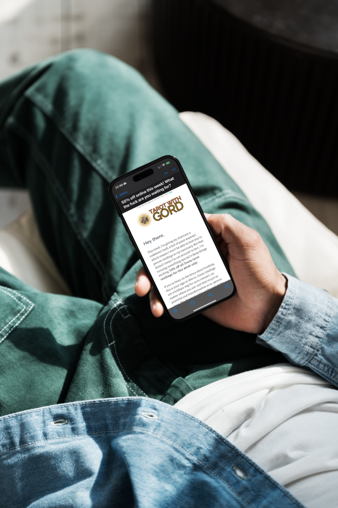 A person lounging on a couch, holding a smartphone displaying an email from tarot with gord, showcasing exclusive offers and updates.