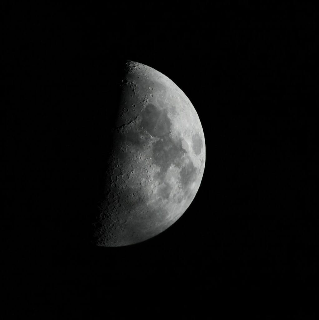 A first quarter moon is shown in the dark sky